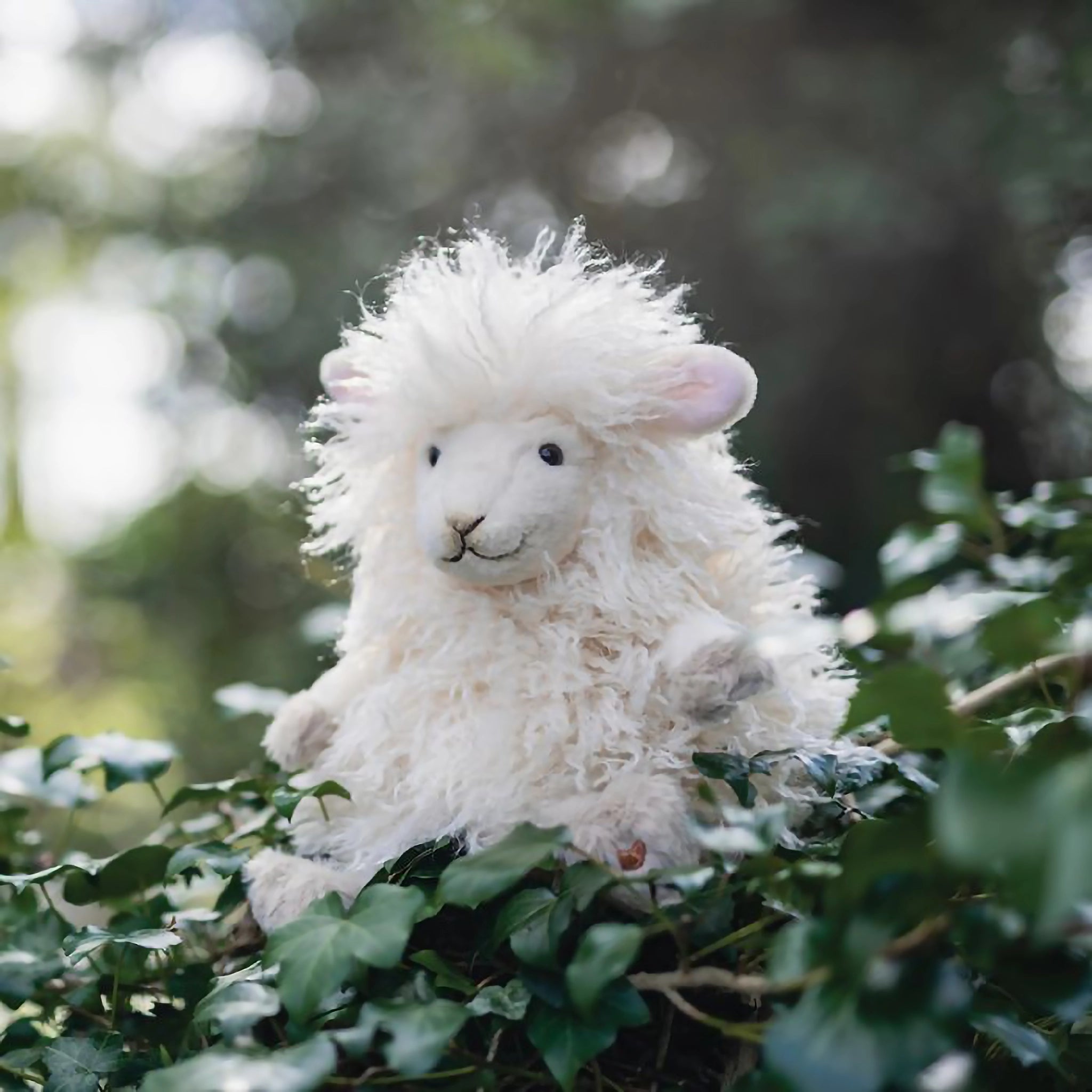 A stuffed sheep plush toy with the Wrendale logo embroidered on the bottom of its foot posed in ivy