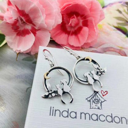 A pair of silver earrings featuring a cat and dog sat together under a gold moon