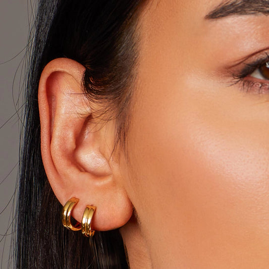 Model wearing a pair of gold huggie hoop earrings with hinge