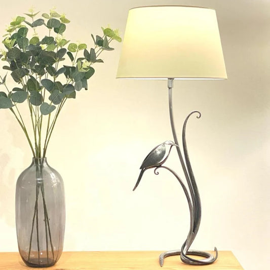 A curved forged steel table lamp with bird detail