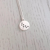 A silver necklace featuring a round pendant with matt texture and a row of cut out bird prints