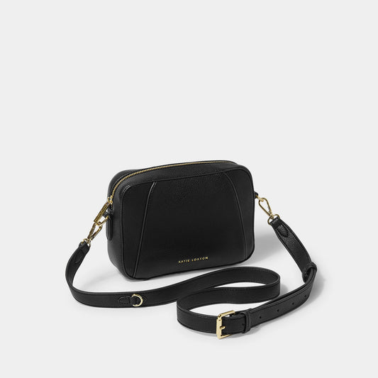 A black crossbody bag in a simple box shape with adjustable strap and gold hardware