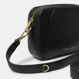 Detail of black crossbody bag in a simple box shape with adjustable strap and gold hardware