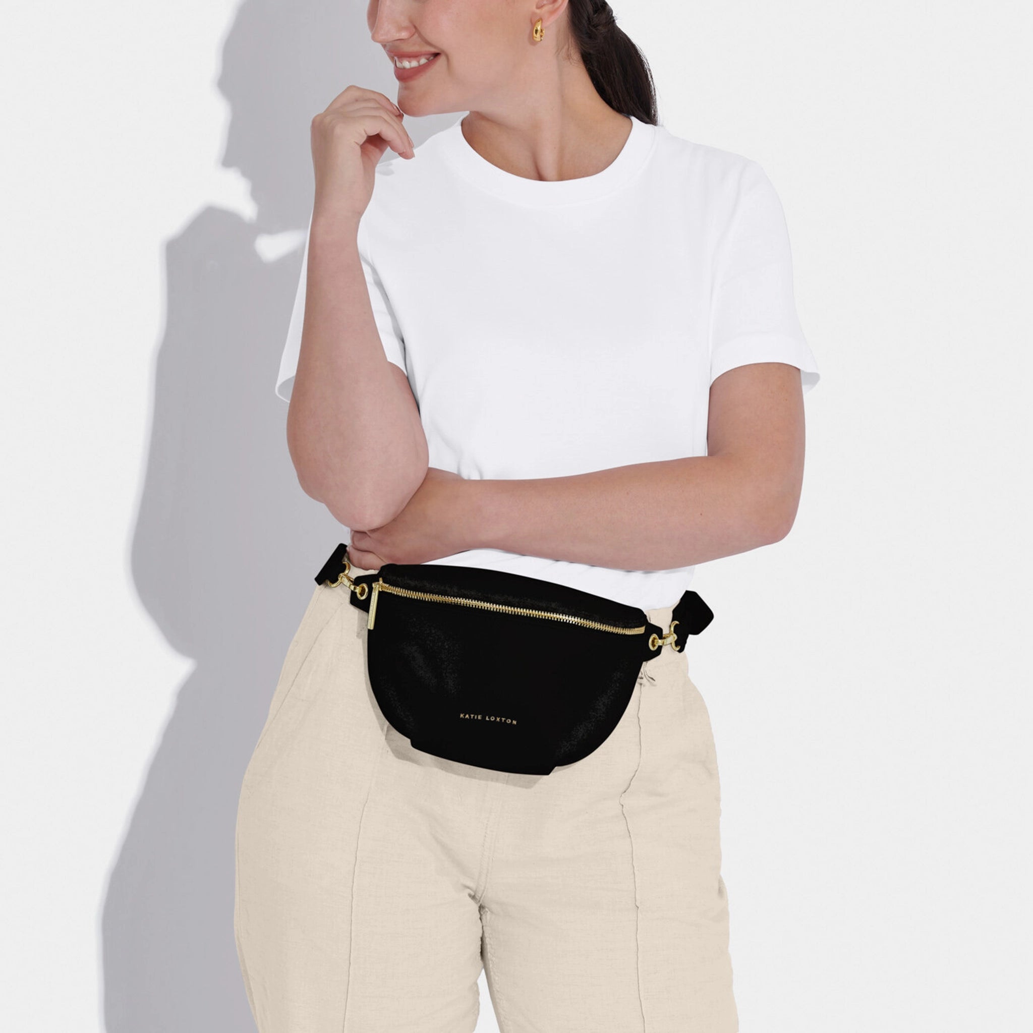 Model wearing a belt bag in faux leather and black with gold hardware