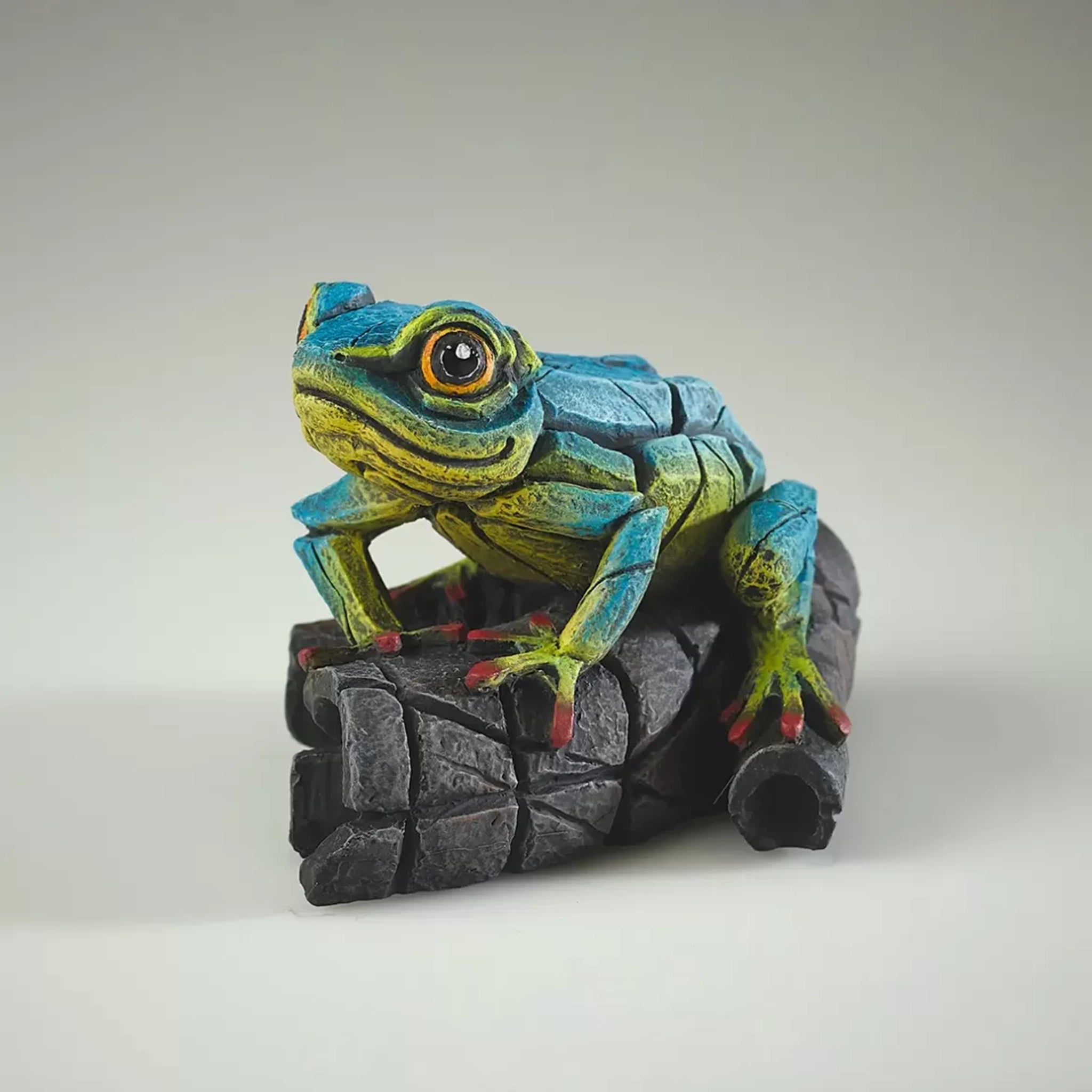 A textured and painted blue and yellow tree frog on log sculpture from side