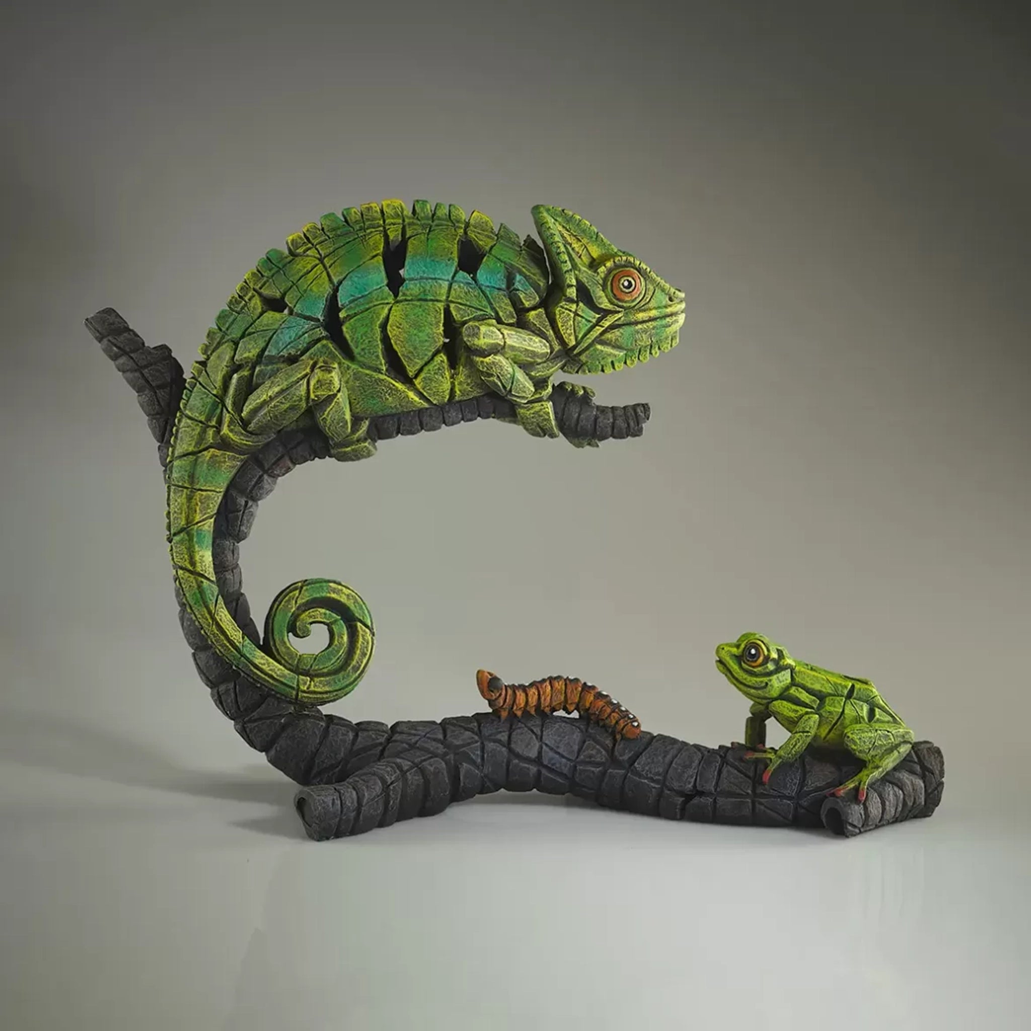 A textured and painted green chameleon on log sculpture with tree frog sculpture