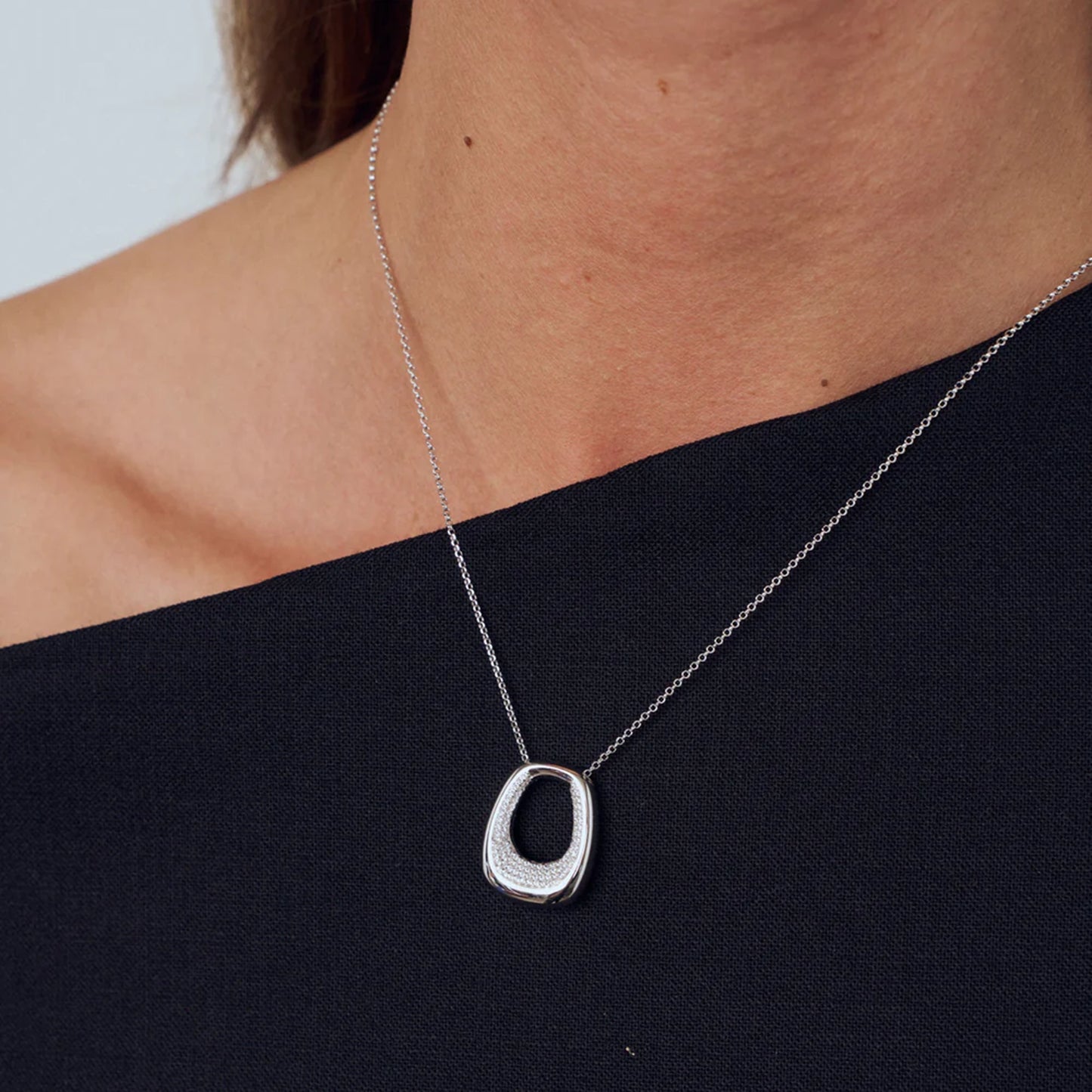 Model wearing an open curved rectangular shaped pendant with CZ stones in the centre opening