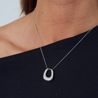 Model wearing an open curved rectangular shaped pendant with CZ stones in the centre opening