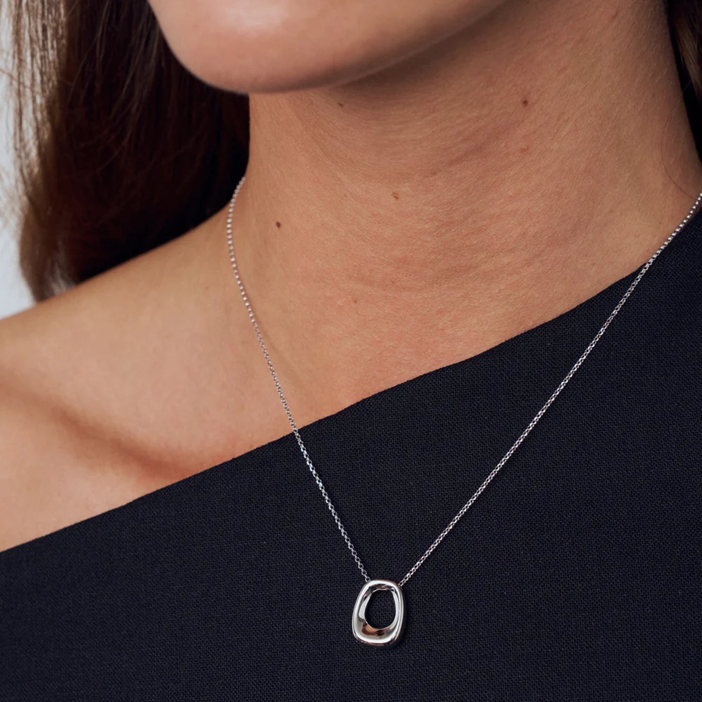 Model wearing modern design silver curved rectangular pendant with open centre on a silver chain