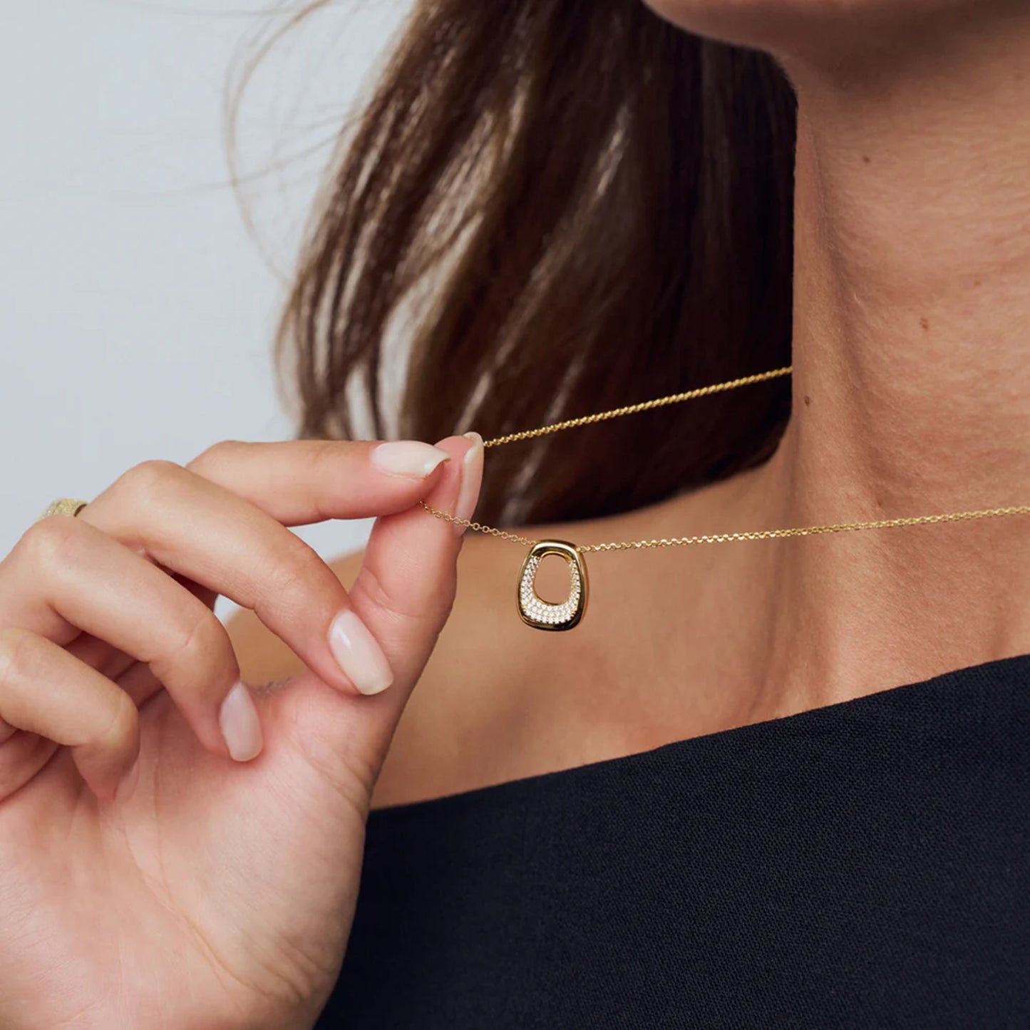 Model wearing open curved rectangular shaped yellow gold pendant with CZ stones in the centre opening 