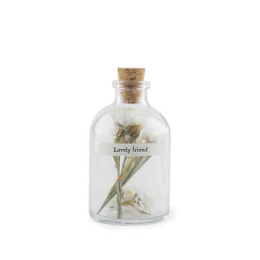 A small cork stopped glass bottle with dried flowers inside and a label that reads 'lovely friend'
