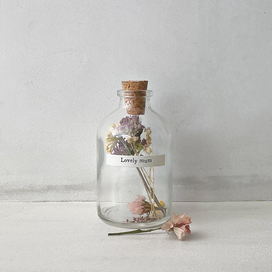 A small cork stopped glass bottle with dried flowers inside and a label that reads 'lovely mum'