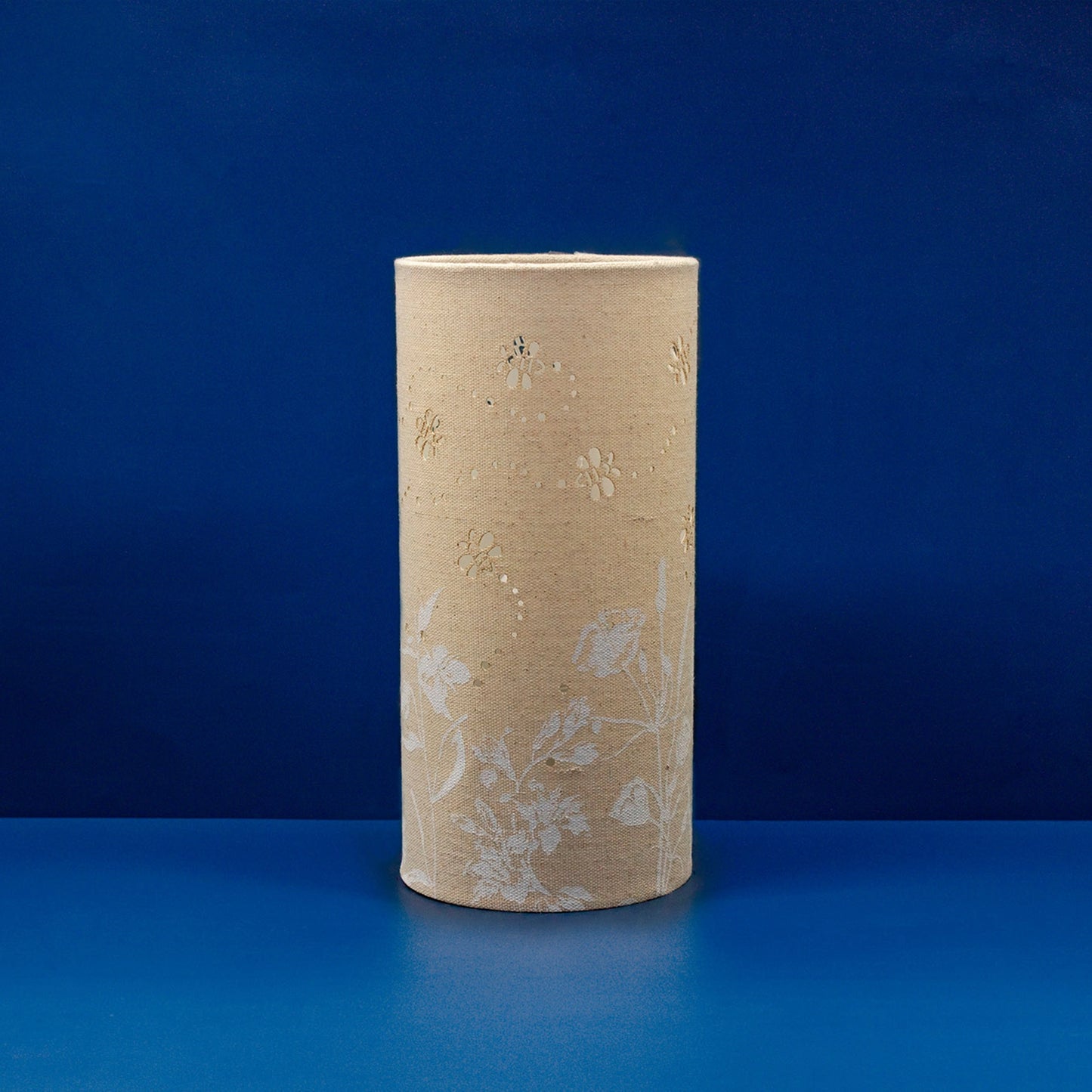 A linen look fabric table lamp with a flower and bumblebee design and cut out leaf details