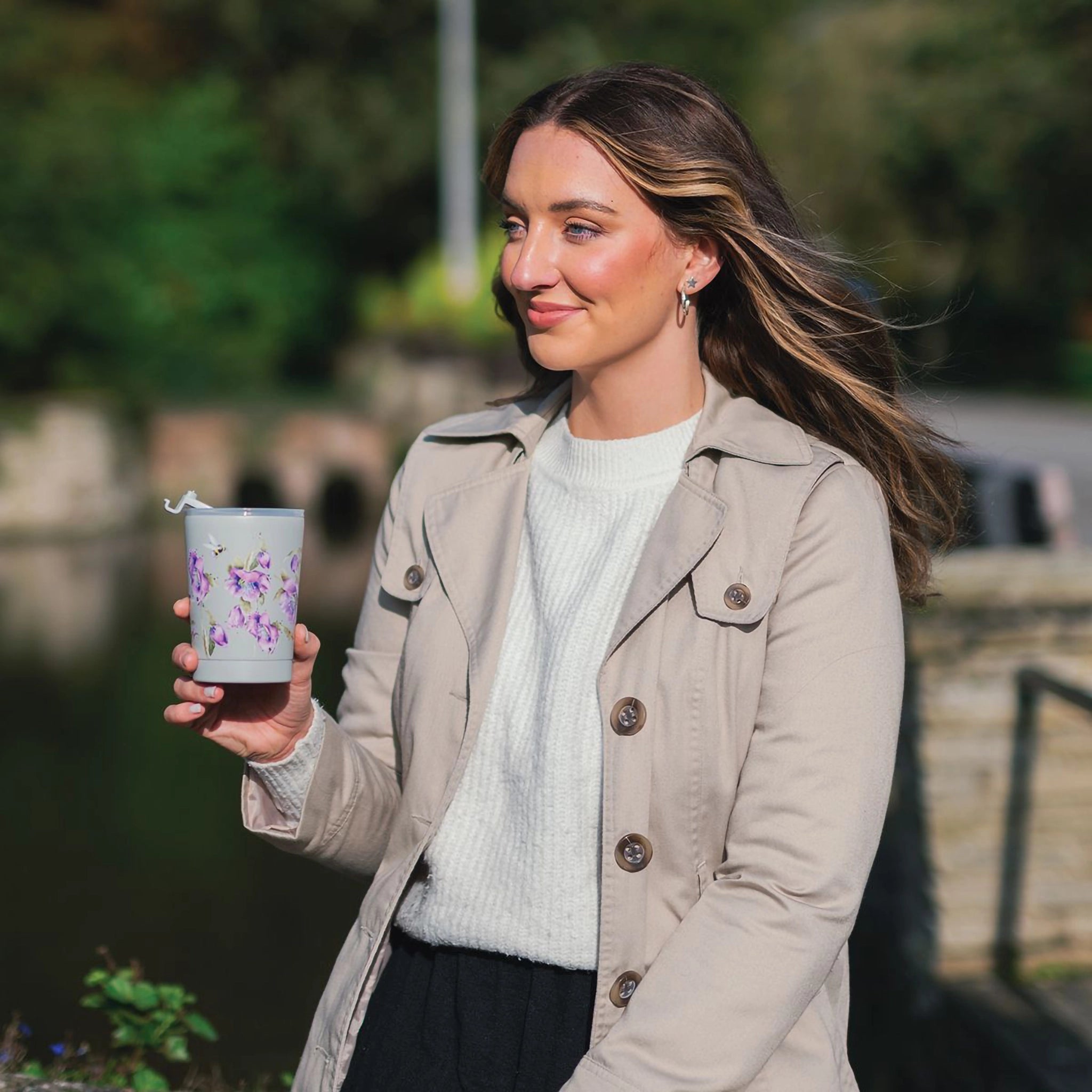 Model holding a grey thermal cup featuring illustrations of bees and purple flowers
