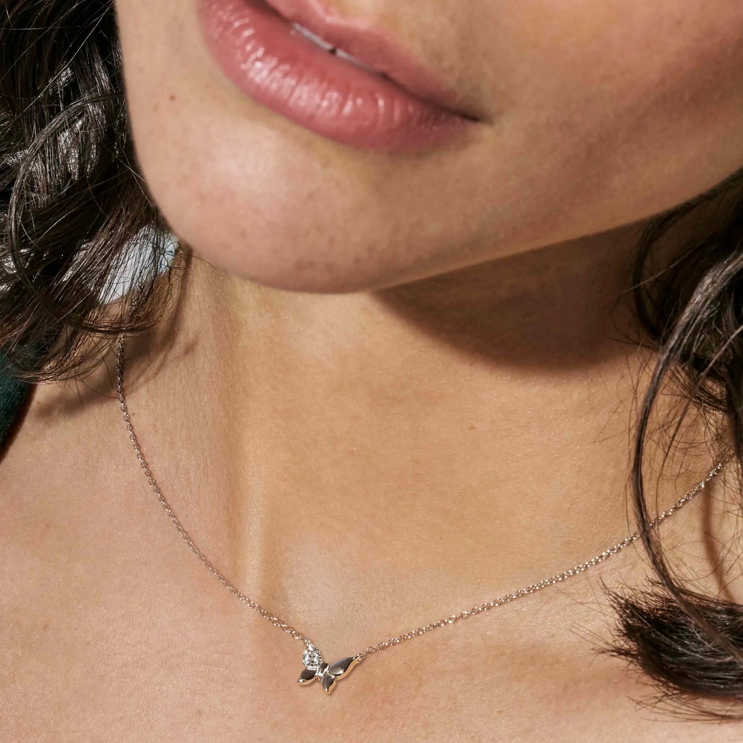 Model wearing silver necklace with butterfly pendant set with pave CZ stones on one wing
