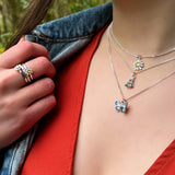 Model wearing stacked small silver pendants, a blue butterfly, bumblebee and daisy on silver chains
