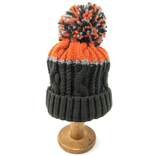 A cable knit hat with green bottom, orange top and a mixed pompom