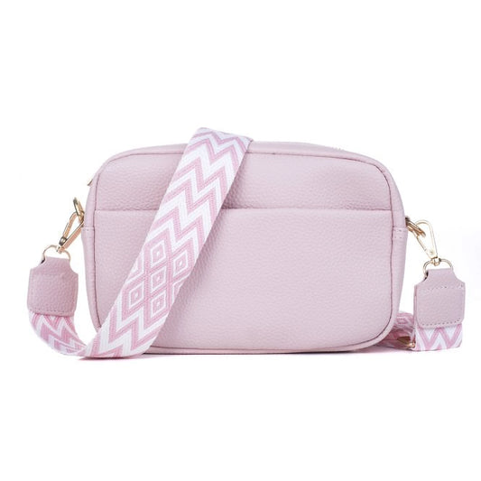 A light pink camera bag with leather texture and a woven geometric patterned strap