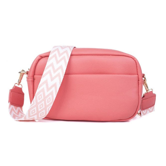 A leather textured camera bag in a vibrant coral pink with woven geometric patterned strap