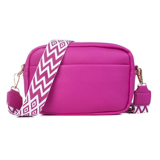 A leather texture camera bag in a vibrant pink with a woven geometric pattern white and pink strap
