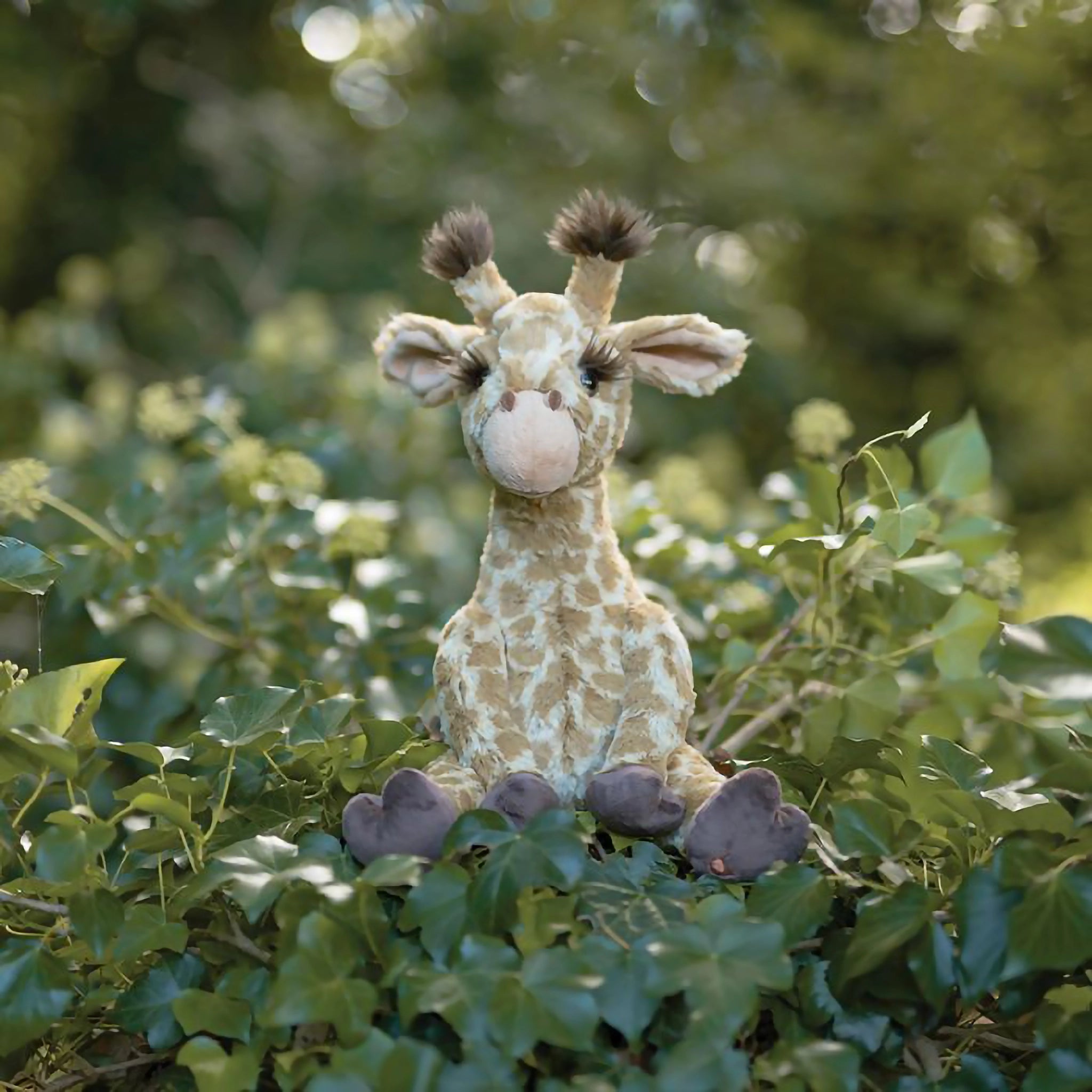 A stuffed giraffe plush toy with the Wrendale logo embroidered on the bottom of its foot posed in ivy
