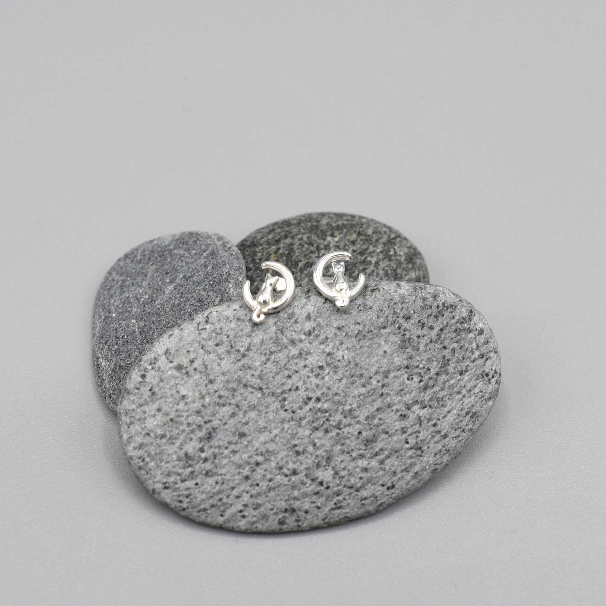 A pair of silver earrings shaped like cats sitting on crescent moons