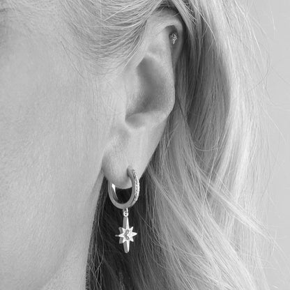 Model wearing a pair of silver hoop earrings with CZ set drop stars