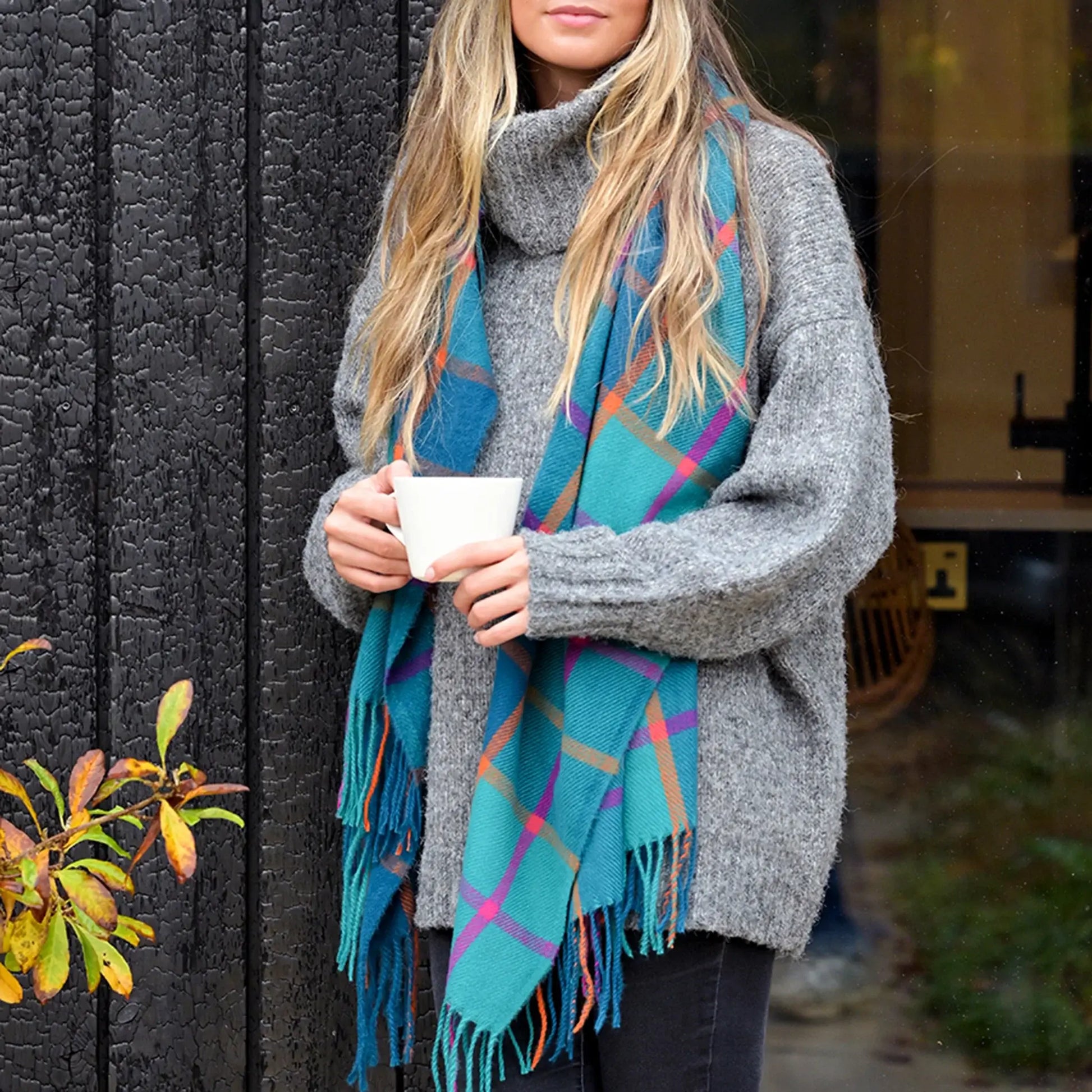 Model wearing teal, purple and orange check scarf with tassel fringe