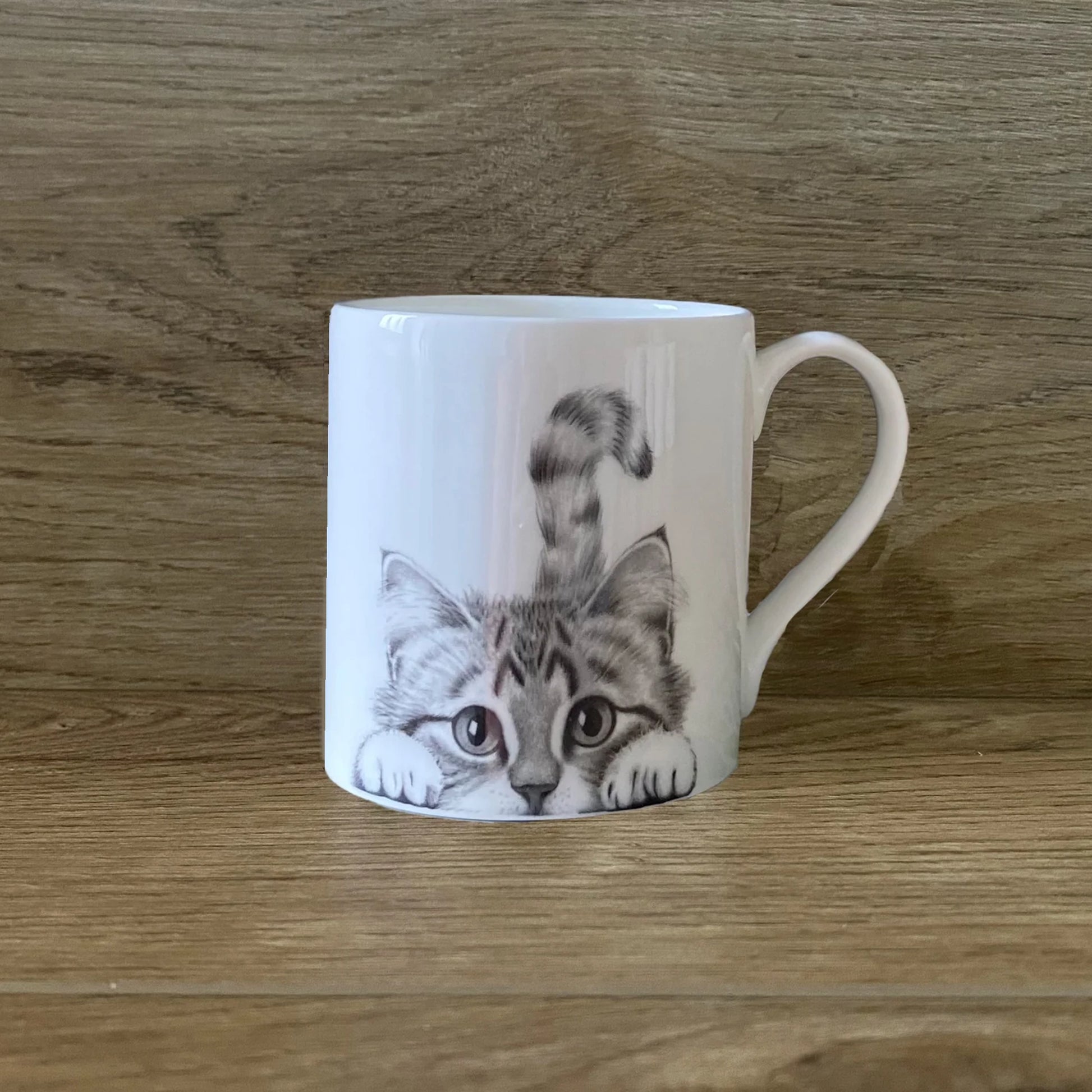 White mug featuring a grey peeking cat illustration 