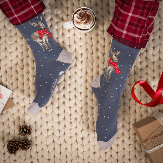 Model wearing a pair of Christmas socks in blue with white heels and toes and a donkey in a scarf in the snow