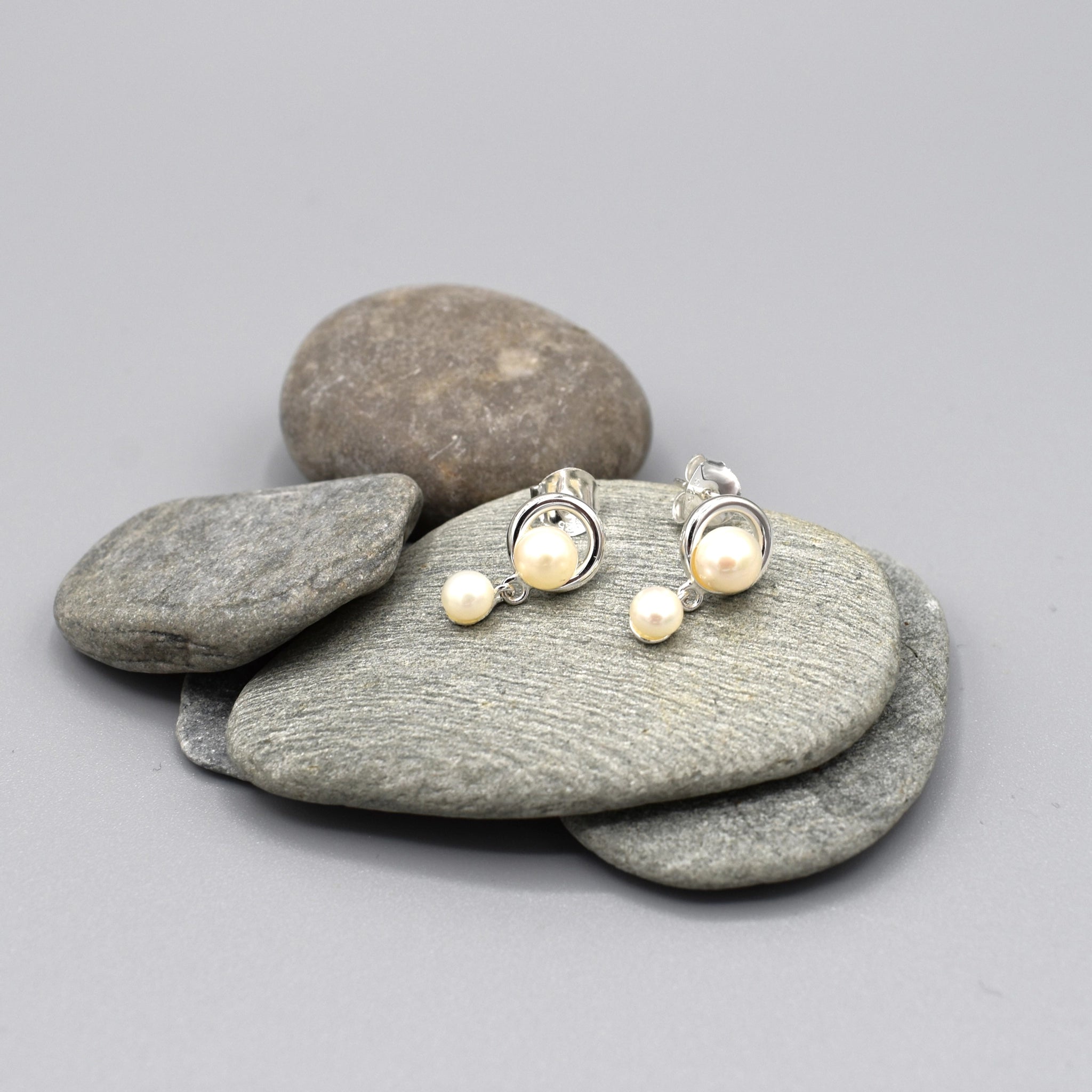 Stud earrings with a simple circle set with a pearl and a smaller drop pearl at the bottom