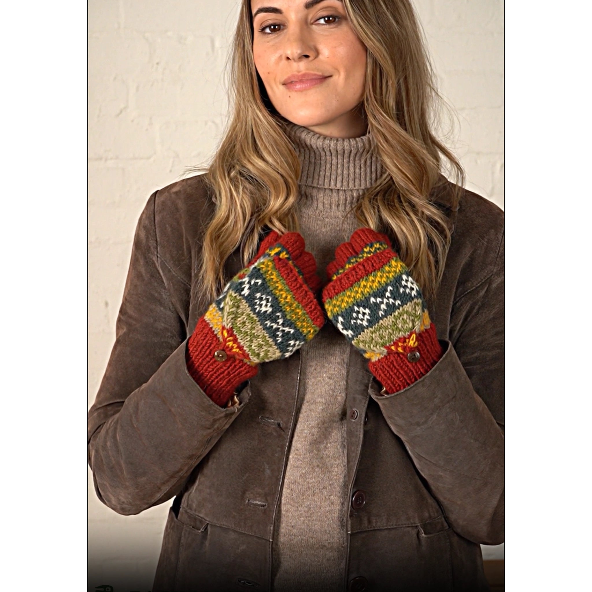 Model wearing a pair of knitted glove mittens with a rust and green fair isle pattern.