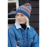 Model wearing a denim pompom beanie hat with multicolour stripe pattern