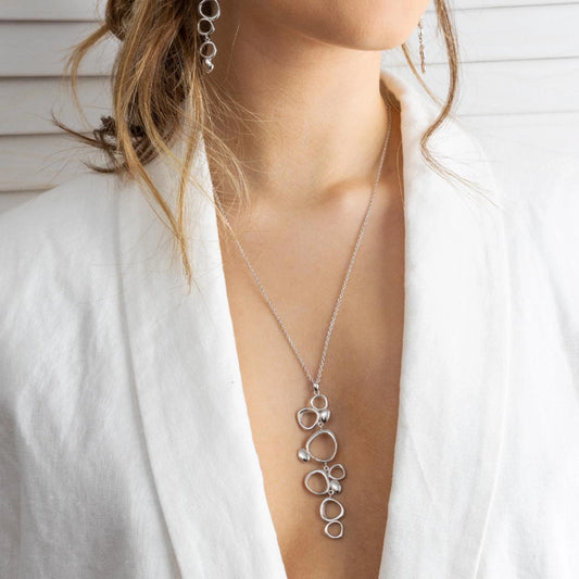 Model wearing a silver pendant featuring a long cascade of pebble shapes in irregular sizes