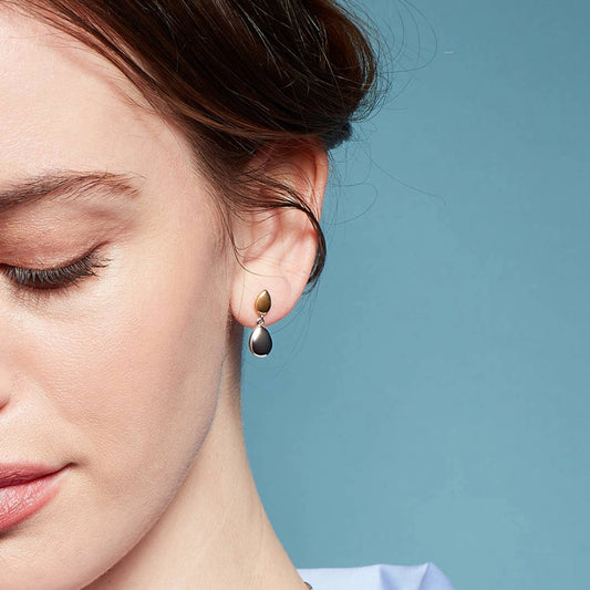 Model wearing pair of drop earrings with two pebble shapes, one in yellow gold and one in silver