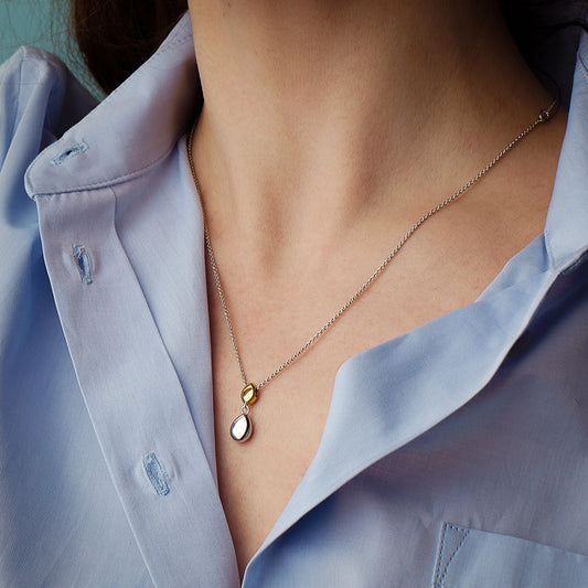 Model wearing a pendant with two pebble shapes, one in yellow gold and one in silver