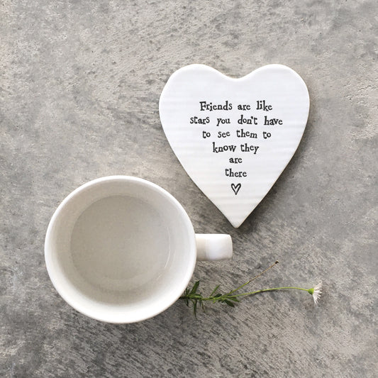 A white ceramic heart shaped coaster featuring a quote and a heart with a mug