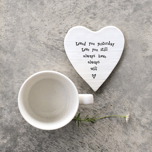 A white ceramic heart shaped coaster featuring a quote and a heart and a mug