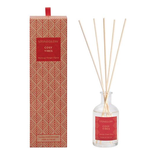 A glass reed diffuser with a box decorated with Scandi style red trees