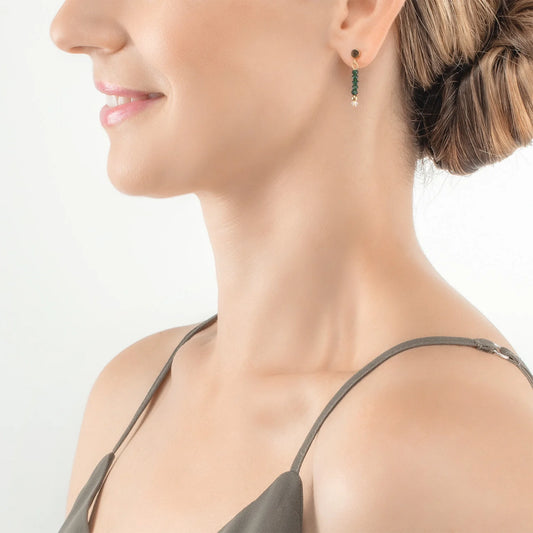 Model wearing a gold pair of earrings with cut dark green glass beads