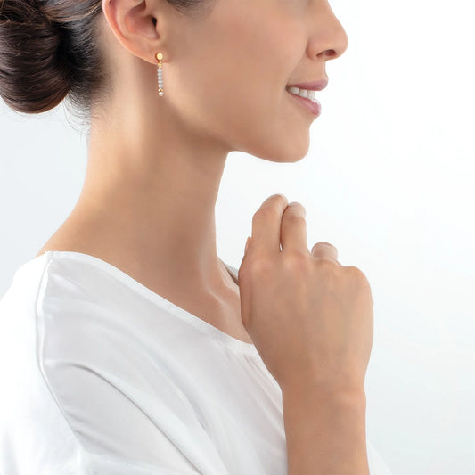 Model wearing a gold pair of earrings with cut ice blue glass beads