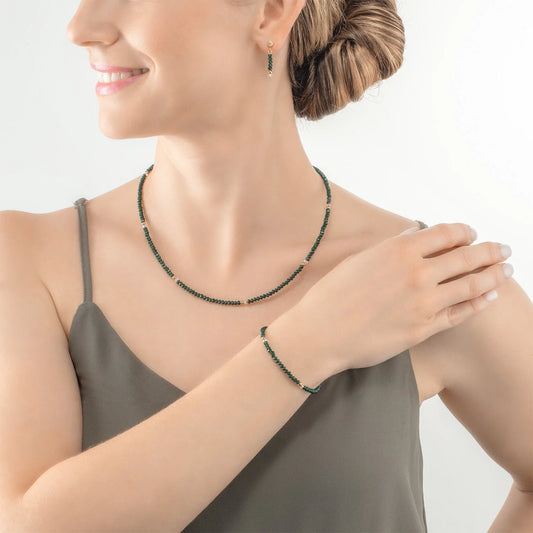 Model wearing a gold necklace and bracelet with cut dark green glass beads