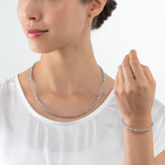 Model wearing a gold necklace and bracelet with cut ice blue glass beads
