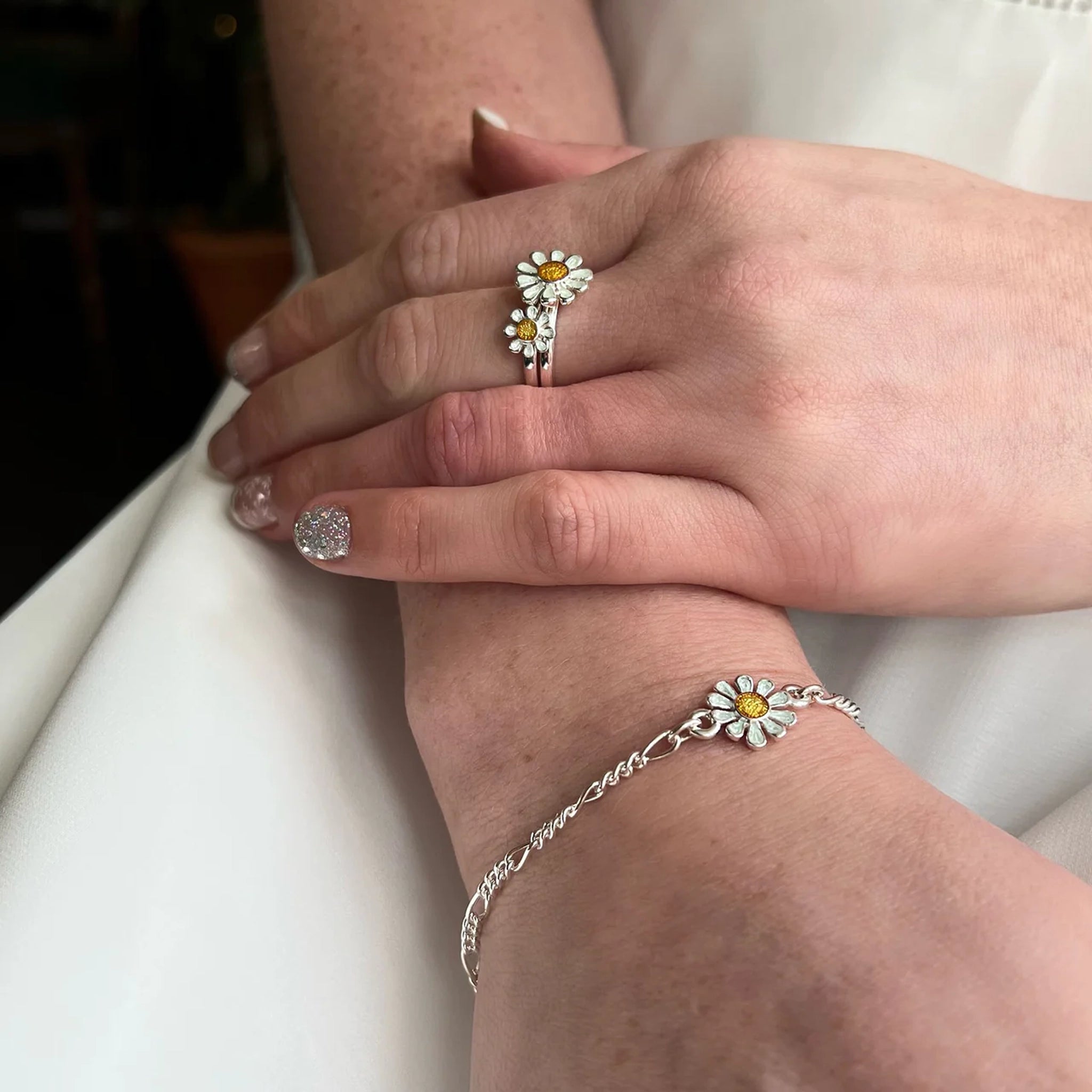 Model wearing a polished silver chain bracelet with daisy pendant in white and yellow enamel