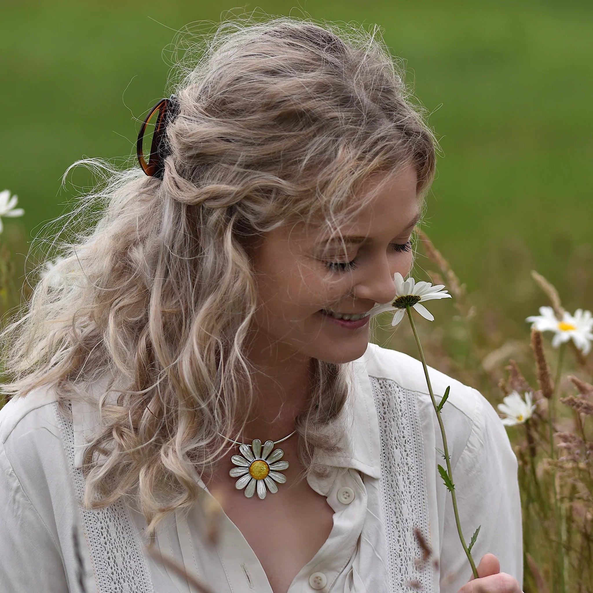 Model wearing polished silver daisy necklet in white and yellow enamel on a silver neck wire in flower field