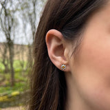 Model wearing polished silver daisy stud earrings with yellow and white enamel