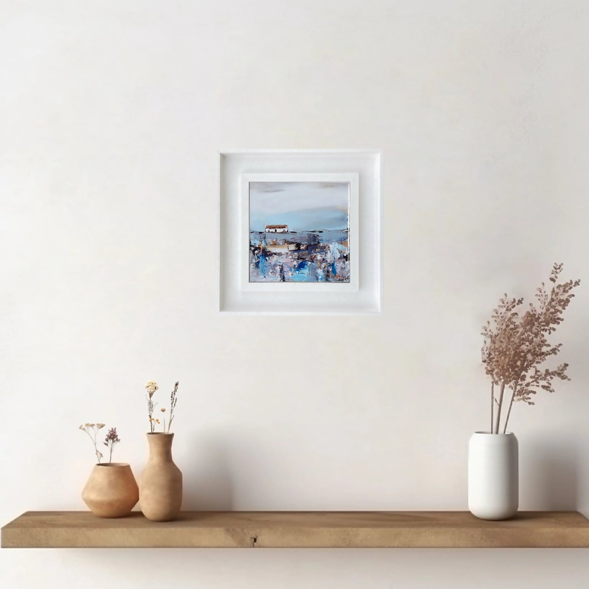 A ceramic tile printed with an abstract painting of a cottage and daisy flowers mounted on a white frame