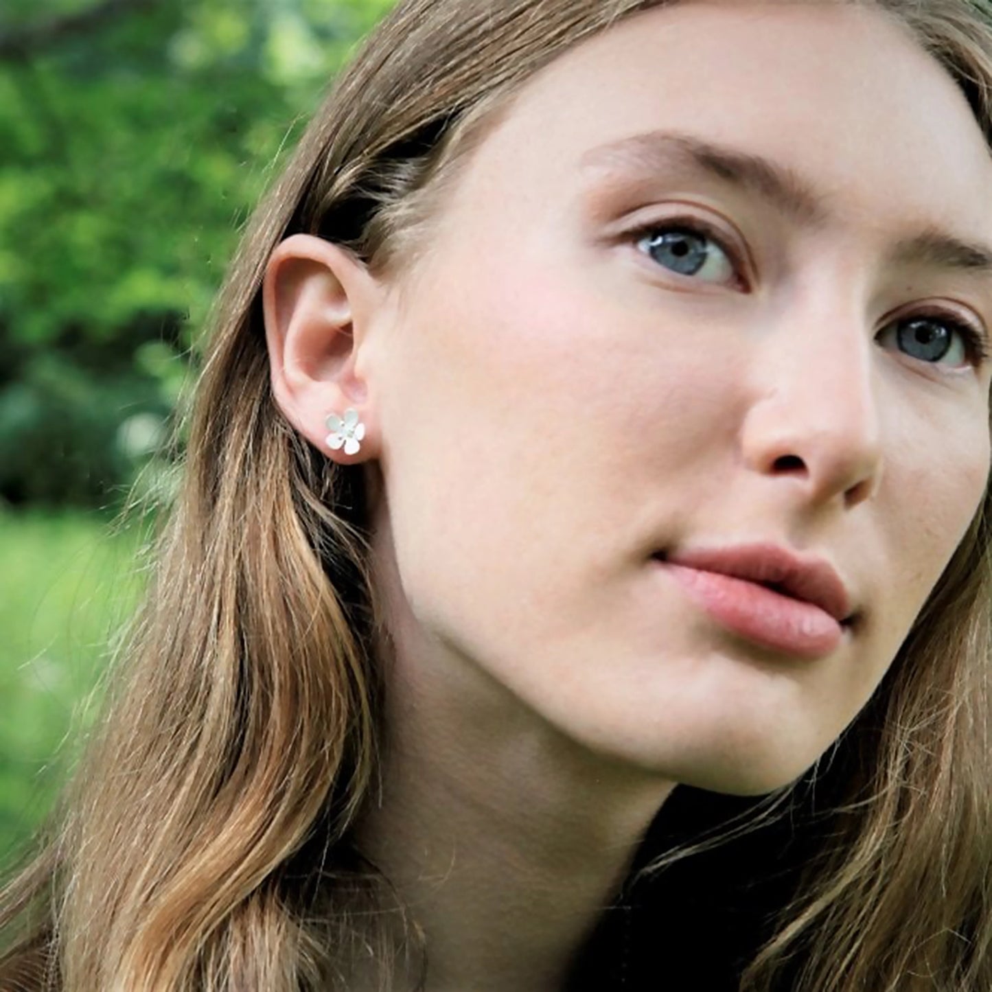 Model wearing satin finish daisy shaped stud earrings with stamen details
