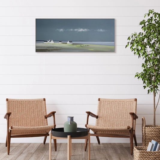 Long framed print of a coastal scene in greens and blues with three white cottages on the horizon hanging in a light room.