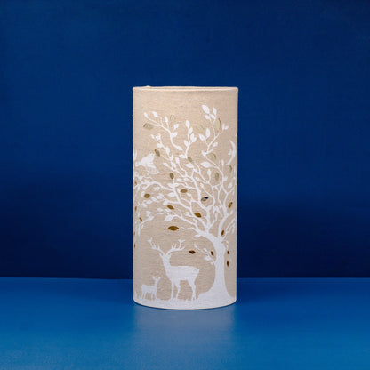 A linen look fabric table lamp with a tree and deer design and cut out leaf details